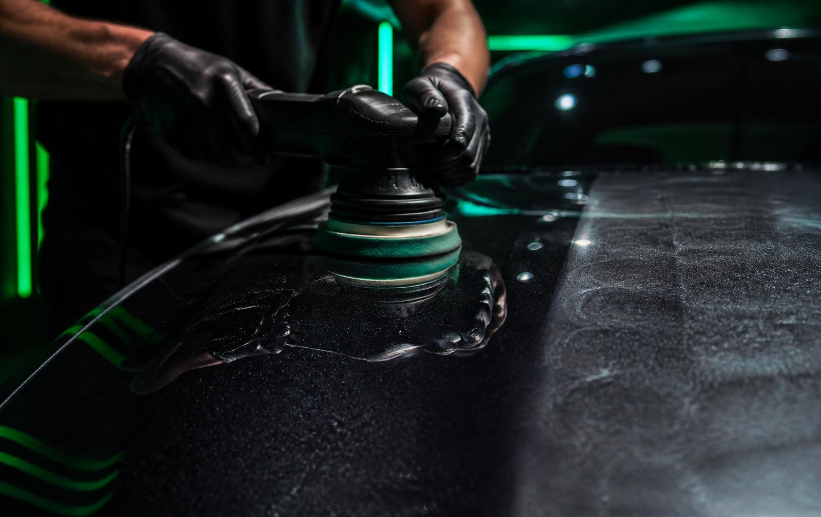 Machine polishing a dark car hood during paint correction