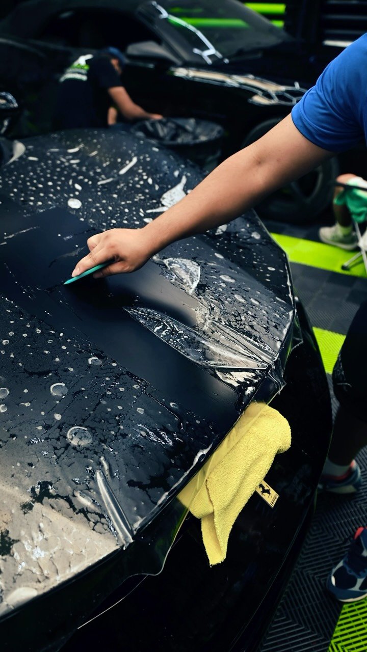 Paint protection film being squeegeed onto a dark exotic vehicle hood